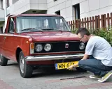 Mężczyzna montuje tablicę rejestracyjną do zabytkowego Fiata 125p. Może to być krok do rejestracji na zabytek bez dokumentów.
