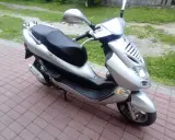 Srebrny skuter Kymco Bet&Win 50 stoi na chodniku z kostki brukowej.