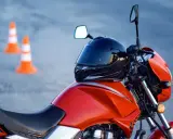 Pomarańczowy motocykl z kaskiem na baku i pachołkami w tle. Czy na motor trzeba mieć prawo jazdy? Tak, do prowadzenia motocykla wymagane jest odpowiednie prawo jazdy.