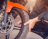 Sprawdzanie, jakie ciśnienie w oponach motocyklowych jest kluczowe dla bezpieczeństwa. Dłoń z manometrem przy wentylu przedniego koła.