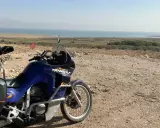 Motocykl Honda Transalp z bagażami gotowy do podróży, z widokiem na Morze Martwe. Dokumenty, jak **carnet de passage**, czekają na przygodę.