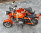 Pomarańczowa motorynka z koszem, ozdobiona płomieniami, gotowa na przejażdżkę.