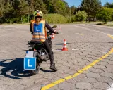 Nauka jazdy motocyklem na placu manewrowym. Osoba w kamizelce odblaskowej z literą "L" na motocyklu.