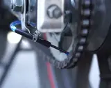 Kropla oleju spada z dyszy systemu automatycznego smarowania łańcucha na ogniwa napędu.