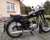 Czarny motocykl z PRL-u, z czerwonym siedzeniem i złotymi ozdobami. Klasyka polskich motocykli.