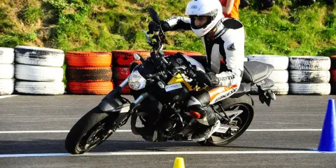 Motocyklista w kombinezonie i kasku wykonuje zakręt, przyjmując sportową pozycję na motocyklu.