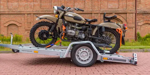 Motocykl Ural zabezpieczony pasami na przyczepie, pokazujący, jak przewieźć motocykl na zwykłej przyczepie.