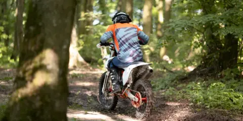 Motocyklista w kasku i pomarańczowej bluzie pędzi leśnym szlakiem. Od ilu lat można jeździć crossem? Odpowiedź zależy od przepisów i umiejętności.