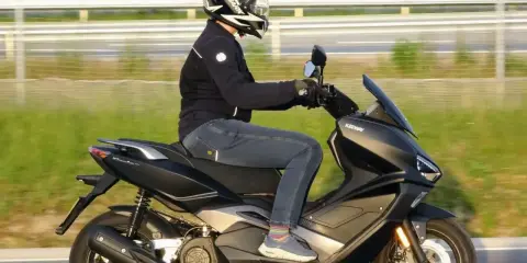 Pierwsze kroki w nauce jazdy na motorze 125. Kierowca w kasku i kurtce jedzie na skuterze Keeway po drodze.