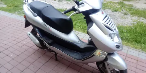 Srebrny skuter Kymco Bet&Win 50 stoi na chodniku z kostki brukowej.