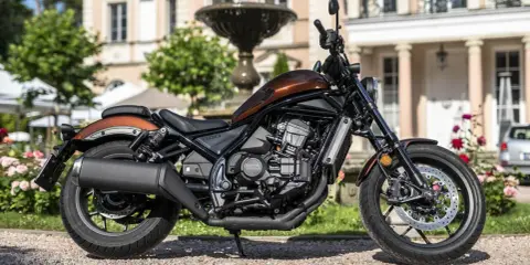 Elegancki, brązowy motocykl Honda Rebel 1100 zaparkowany przed pałacem.