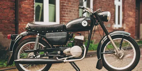 Czarny motocykl wsk 125 na tle ceglanego budynku. Klasyk z PRL-u gotowy do jazdy.