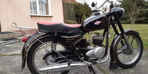 Czarny motocykl z PRL-u, z czerwonym siedzeniem i złotymi ozdobami. Klasyka polskich motocykli.
