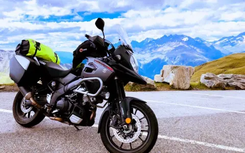 Szary motocykl Suzuki V-Strom, idealny motocykl do turystyki we dwoje, zaparkowany na tle majestatycznych gór i błękitnego nieba.