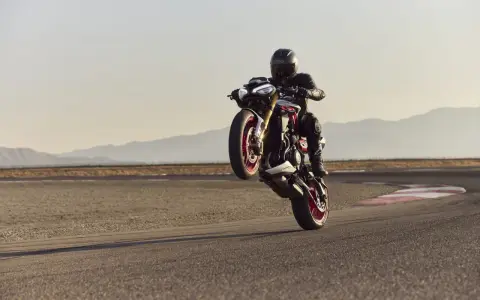 Motocyklista na torze wykonuje wheelie. System kontroli trakcji co to? Pomaga utrzymać przyczepność podczas takich manewrów.