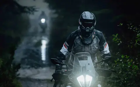 Motocyklista w kasku i kurtce Leatt przemierza leśną drogę w deszczu. Jazda na motocyklu w trudnych warunkach.