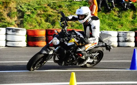 Motocyklista w kombinezonie i kasku wykonuje zakręt, przyjmując sportową pozycję na motocyklu.