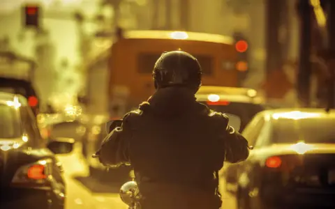 Motocyklista w kasku i kurtce w korku miejskim. Czy motor może jechać między samochodami? Tak, ten motocyklista próbuje.