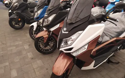 Kilka skuterów, w tym brązowy zipp qr max 125, stoi na chodniku.