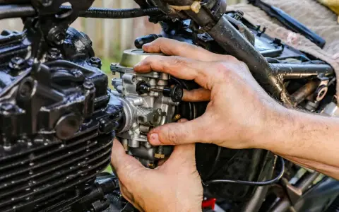 Dłonie mechanika regulują gaźnik motocykla, gdy ssanie jest włączone.