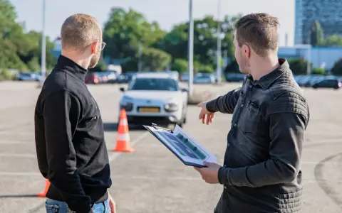 Instruktor omawia z kursantem plan trasy, świętując jego pozytywny wynik egzaminu teoretycznego.