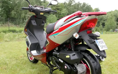 Czerwony skuter 50cc na trawie. Zastanawiasz się, ile jedzie skuter 50 bez blokad? Ten model wygląda na gotowy do szybkiej jazdy!