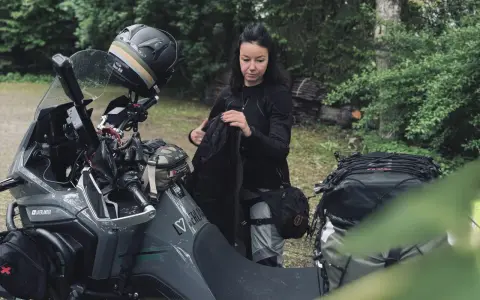 Kobieta pakuje plecak na motocykl. Zastanawia się, co zabrać na wyprawę motocyklową, by niczego nie zapomnieć.