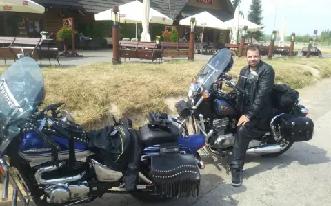 Motocyklista w skórzanej kurtce i spodniach odpoczywa przy swoim motocyklu. W tle karczma "Bida", idealne miejsce na postój podczas odkrywania **tras motocyklowych lubelskich**.