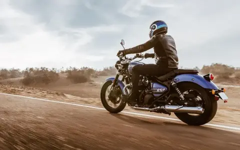 Motocyklista w skórzanej kurtce pędzi na niebieskim **super meteor 650** przez pustynny krajobraz.
