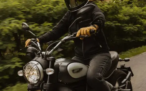 Motocyklista w kasku i żółtych rękawicach jedzie motocyklem. Zastanawia się, przy jakich obrotach zmieniać biegi, by jazda była płynna.