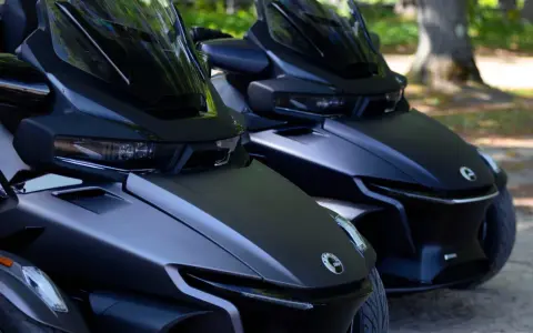 Dwa matowe, czarne pojazdy typu Can-Am Spyder stoją obok siebie na parkingu dla motocykli, gotowe do jazdy.