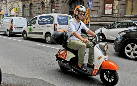 Mężczyzna w kasku jedzie skuterem elektrycznym, przygotowując się do testu na kartę motorowerową.