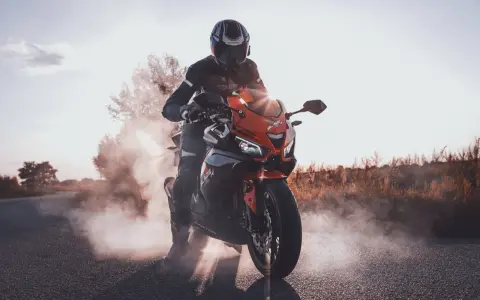 Motocyklista w kasku i kombinezonie na pomarańczowym Barton Blade 125, z którego unosi się dym. Zastanawiasz się, ile pali motor 125?