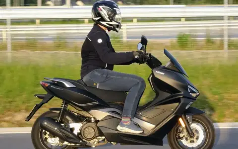 Pierwsze kroki w nauce jazdy na motorze 125. Kierowca w kasku i kurtce jedzie na skuterze Keeway po drodze.