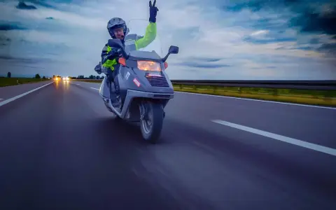 Motocyklista na skuterze 125 pozdrawia z autostrady, pokazując, że można nim jeździć po autostradzie.