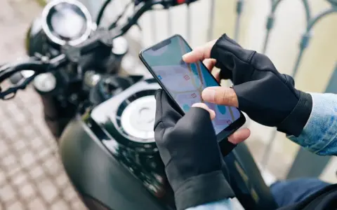 Motocyklista w rękawiczkach sprawdza trasę na mapie w aplikacji dla motocyklistów.