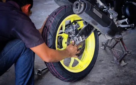 Mechanik dokonuje wymiany opon motocyklowych, pracując przy żółtej feldze i hamulcach.