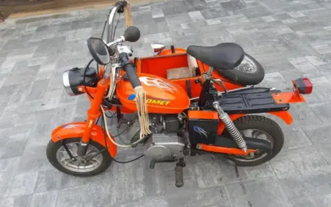 Pomarańczowa motorynka z koszem, ozdobiona płomieniami, gotowa na przejażdżkę.