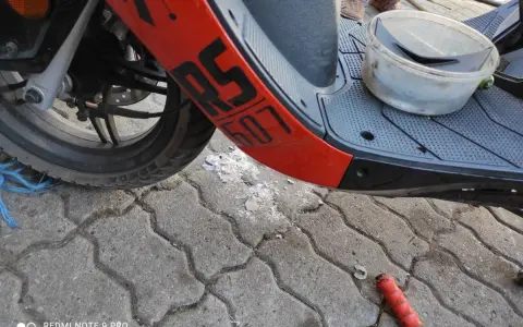 Część skutera Junak 607 4T z pomarańczowym elementem i napisem "607". Na podłodze leżą części i pojemnik.