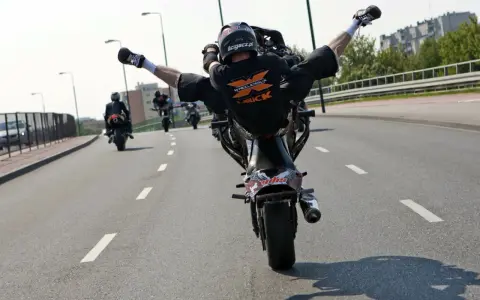 Motocyklista wykonuje jazdę na jednym kole z nogami w powietrzu. Ryzykowne wyczyny mogą skończyć się mandatem.