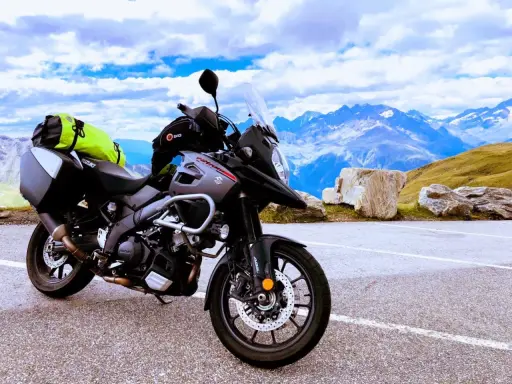 Szary motocykl Suzuki V-Strom, idealny motocykl do turystyki we dwoje, zaparkowany na tle majestatycznych gór i błękitnego nieba.