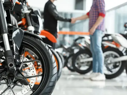 Dwóch mężczyzn ściska sobie dłonie przy motocyklach. Sfinalizowali sprzedaż motocykla przed upływem 6 miesięcy.