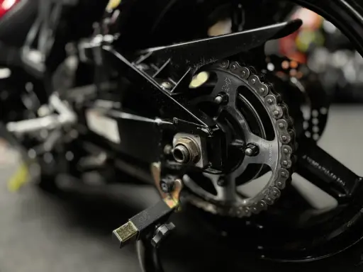 Zbliżenie na tylne koło motocykla z widocznym łańcuchem i zębatką. Pytanie: jaki smar do łańcucha motocyklowego?