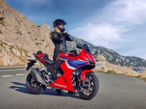 Kobieta w kasku i skórzanej kurtce przy czerwonym motocyklu Honda. Widok na góry i morze. Idealny na najszybsze motocykle na A2.