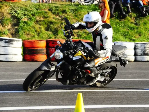 Motocyklista w kombinezonie i kasku wykonuje zakręt, przyjmując sportową pozycję na motocyklu.