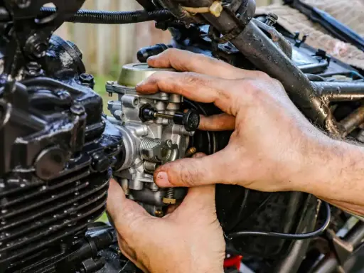 Dłonie mechanika regulują gaźnik motocykla, gdy ssanie jest włączone.
