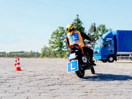 Osoba na motocyklu z literą "L" na kamizelce i tablicy, ćwiczy jazdę. Mam prawo jazdy B, chcę zrobić A.