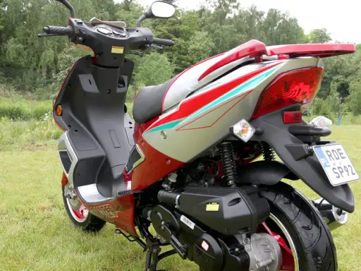 Czerwony skuter 50cc na trawie. Zastanawiasz się, ile jedzie skuter 50 bez blokad? Ten model wygląda na gotowy do szybkiej jazdy!