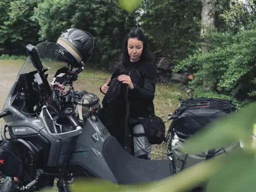 Kobieta pakuje plecak na motocykl. Zastanawia się, co zabrać na wyprawę motocyklową, by niczego nie zapomnieć.