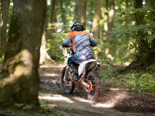Motocyklista w kasku i pomarańczowej bluzie pędzi leśnym szlakiem. Od ilu lat można jeździć crossem? Odpowiedź zależy od przepisów i umiejętności.